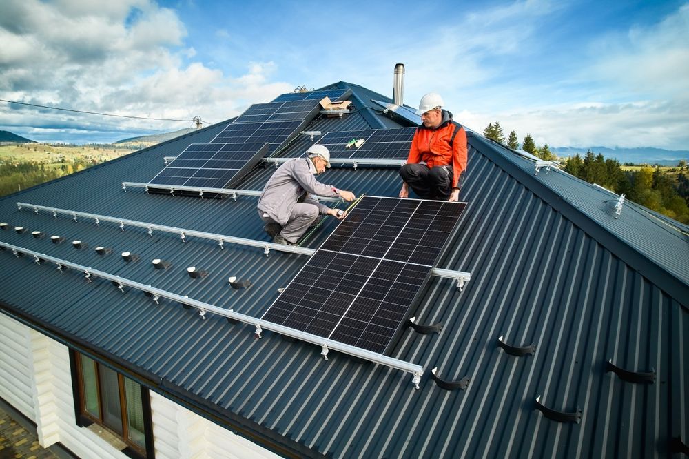 A person installing a solar panel on a gray corrugated metal roof.