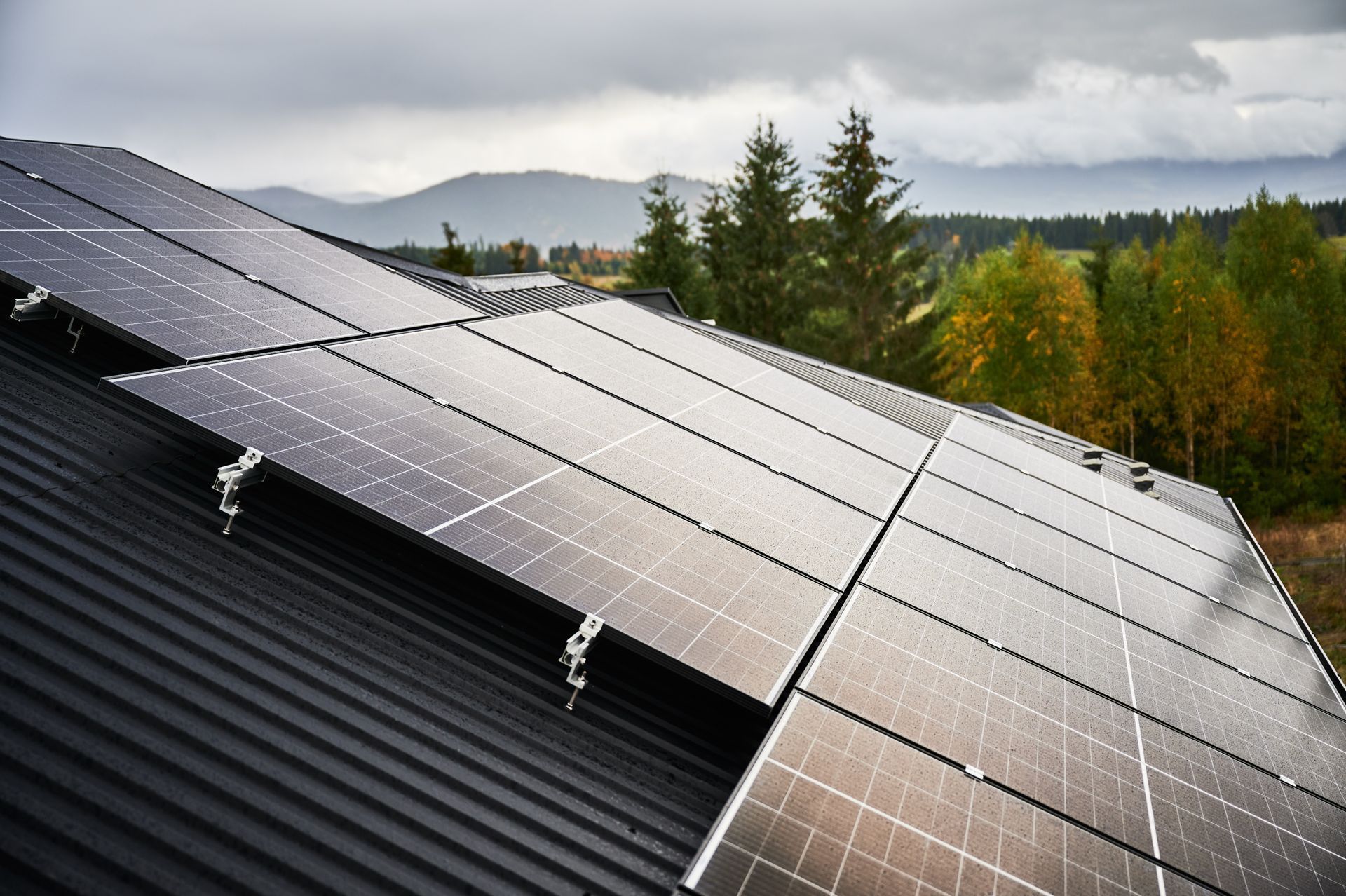 Solar panels on a black rooftop with a forest and mountain backdrop.