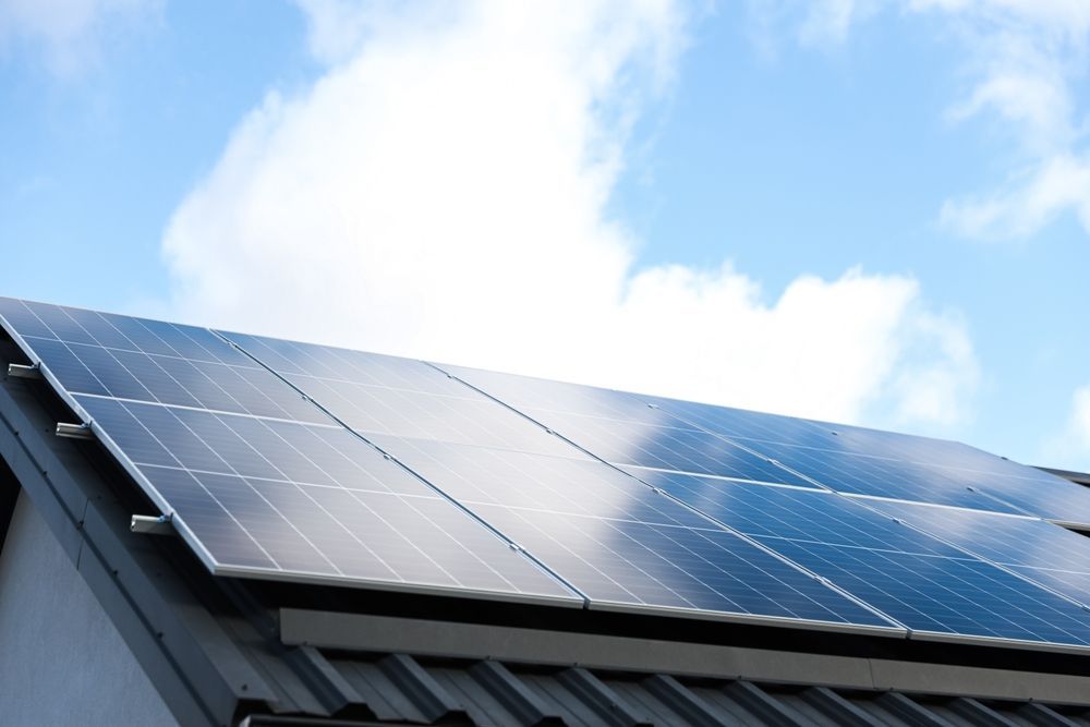 A person installing a solar panel on a gray corrugated metal roof.