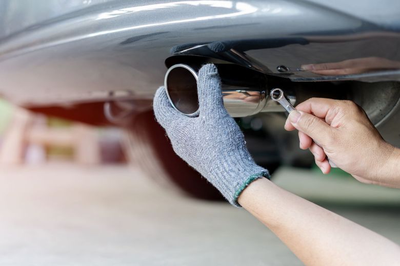 A person is fixing a car exhaust pipe with a wrench.