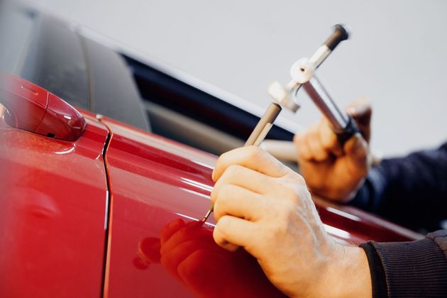 A man is repairing a red car with a wrench.