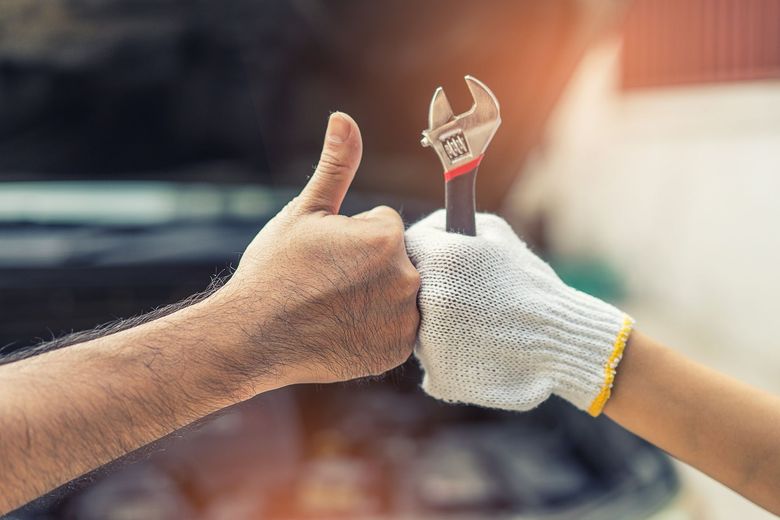 A man and a woman are holding a wrench and giving a thumbs up.
