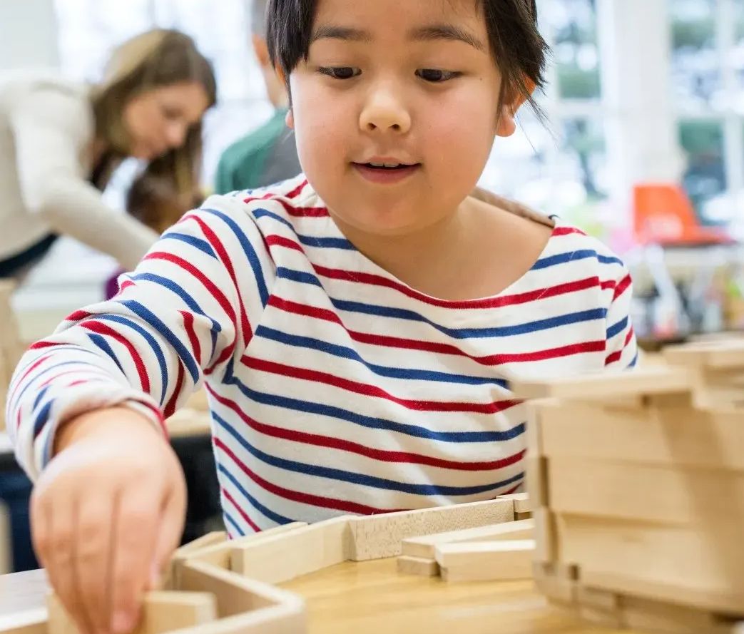 a little girl in a striped shirt is playing with wooden blocks on a table in a classroom
