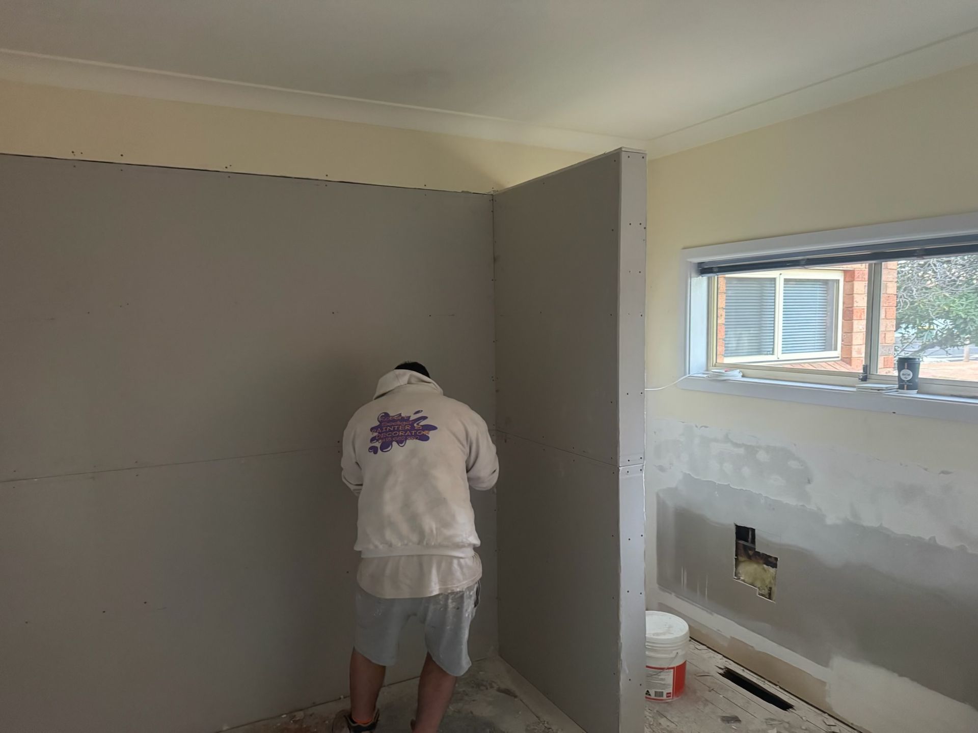 Person Painting a Gray Wall in a Room Under Renovation — Robert Seeliger Painter And Decorator in Warren, NSW