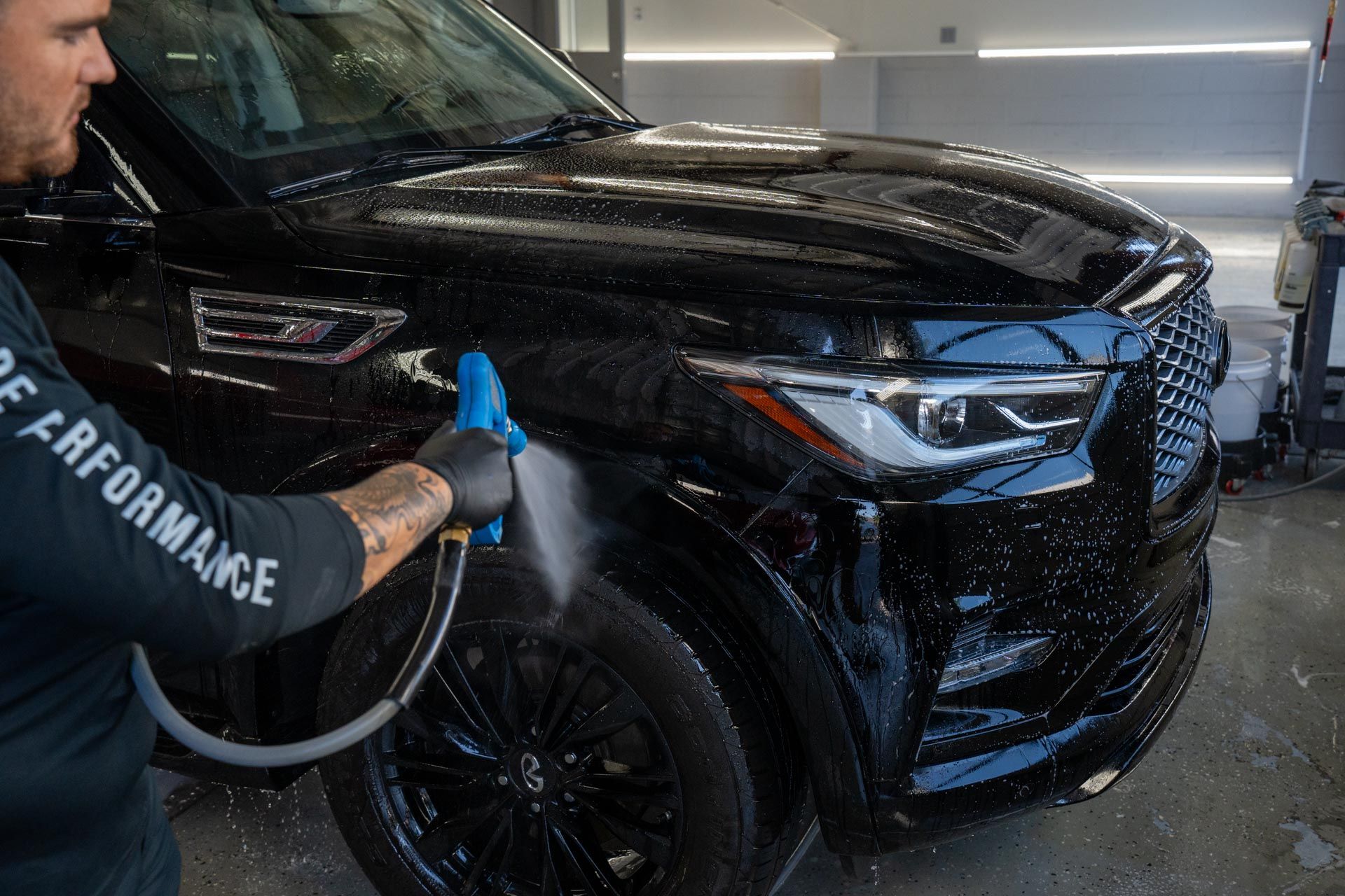 Person washing a black SUV with a hose in a car wash bay.