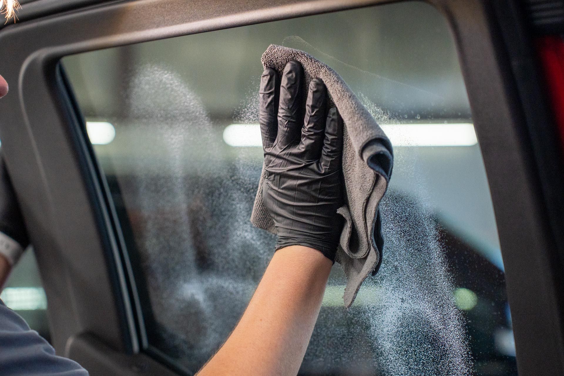 Person wiping car window with gray cloth and wearing black gloves.