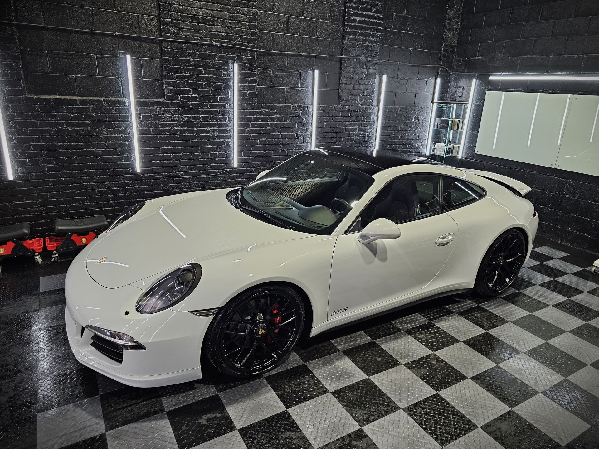 A white porsche 911 is parked in a garage with a checkered floor.
