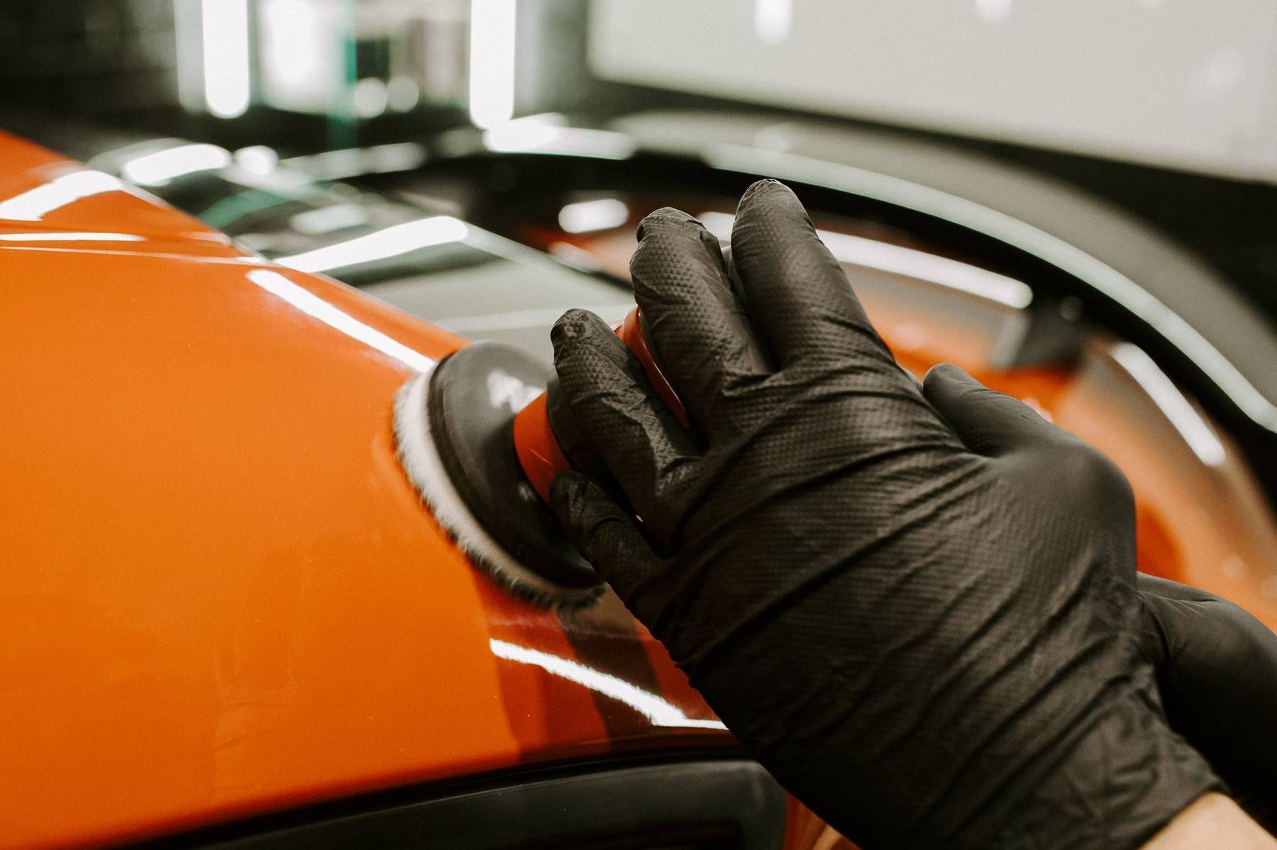 Man wearing gloves cleaning a red car's interior with a microfiber cloth and spray bottle.