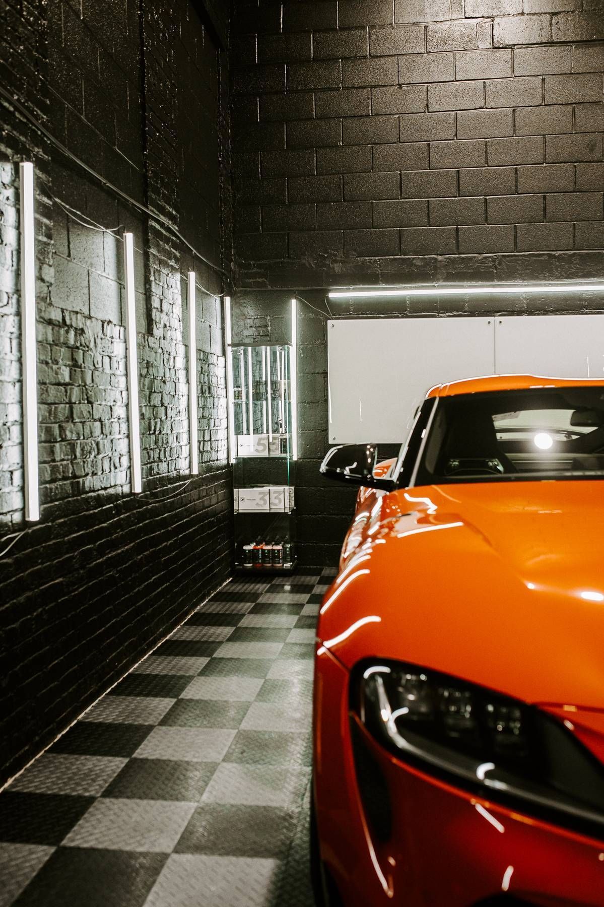 Orange sports car in a black-tiled garage with white accent lighting.