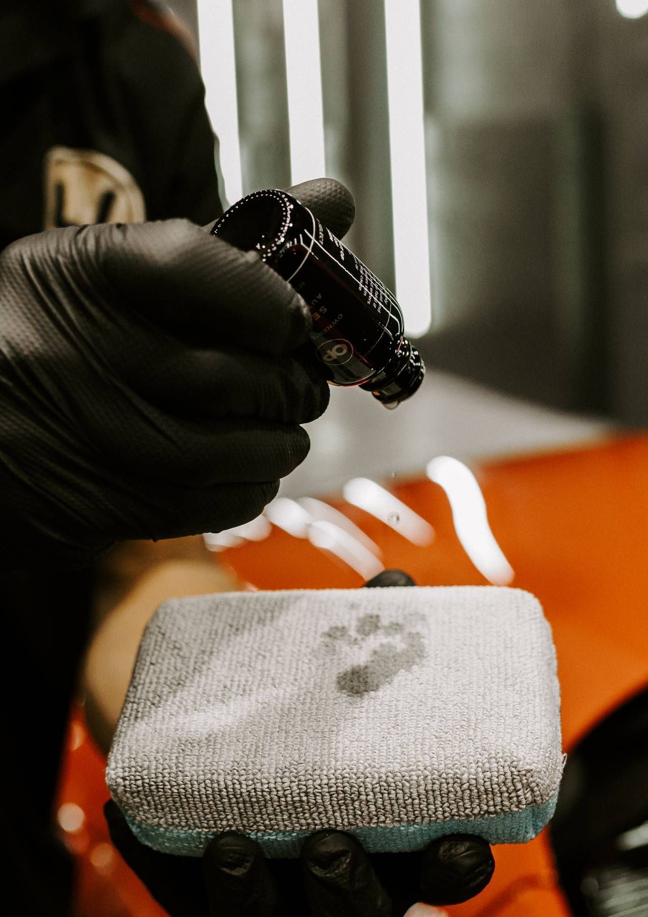 A person wearing black gloves is holding a sponge and a spray bottle.