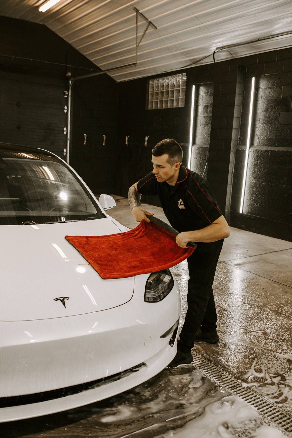 Man drying a white Tesla with a red cloth in a car wash bay.
