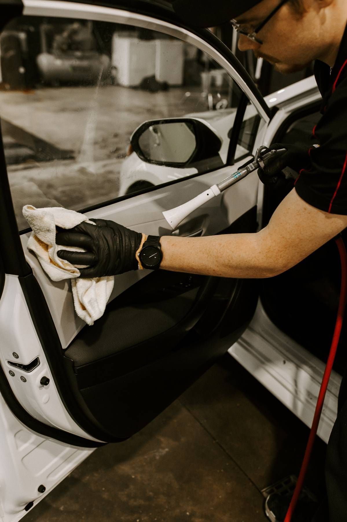 Person in black gloves cleaning a car door with a white cloth and tool.