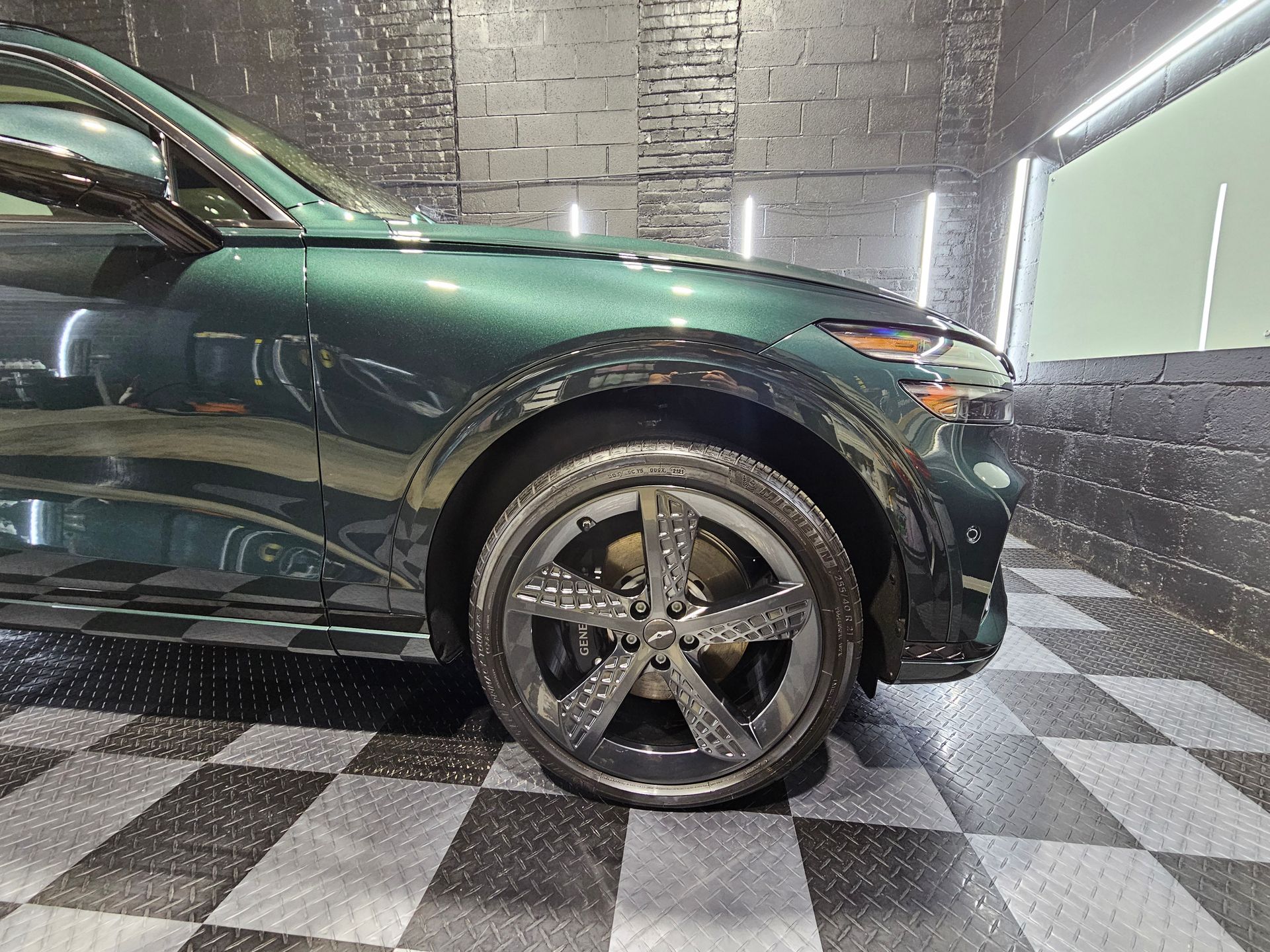 A green car is parked in a garage with a checkered floor.