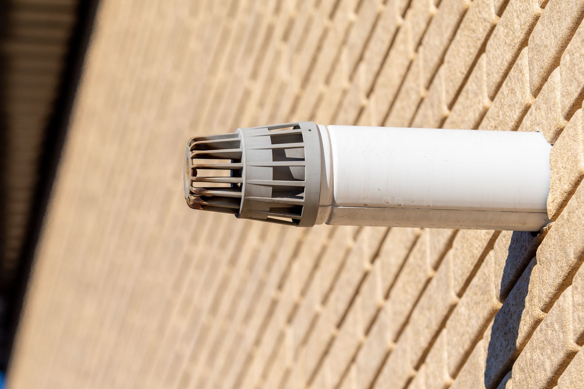 A white pipe is attached to a brick wall.
