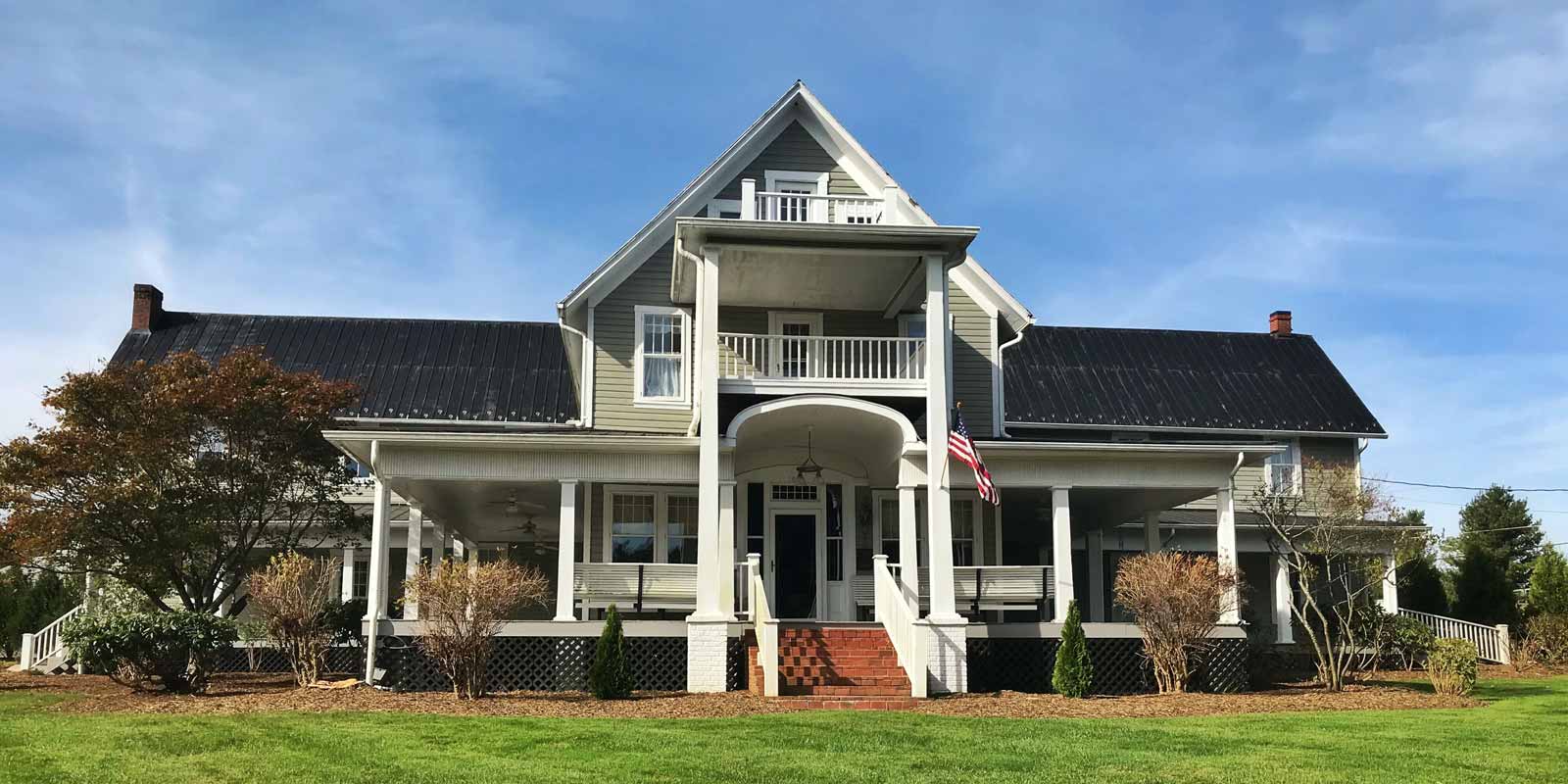 A large white house with a black roof is sitting on top of a lush green field.