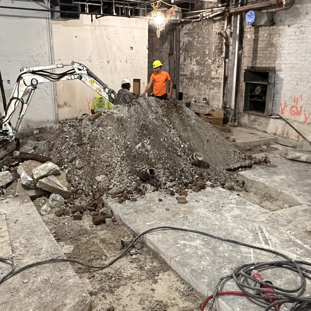 A man is standing next to a pile of concrete excavated dirt and conrete in a building.