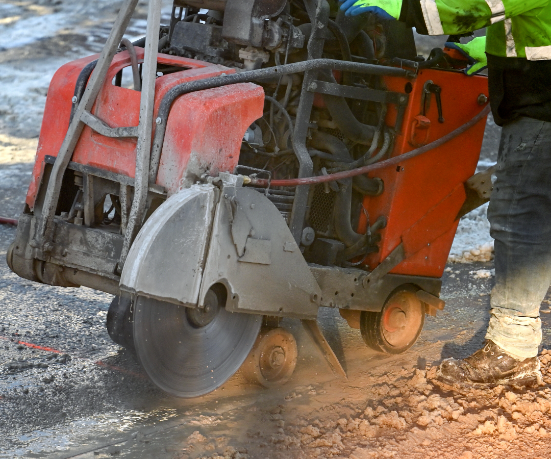 A man is using a concrete saw to cut a hole in the ground.