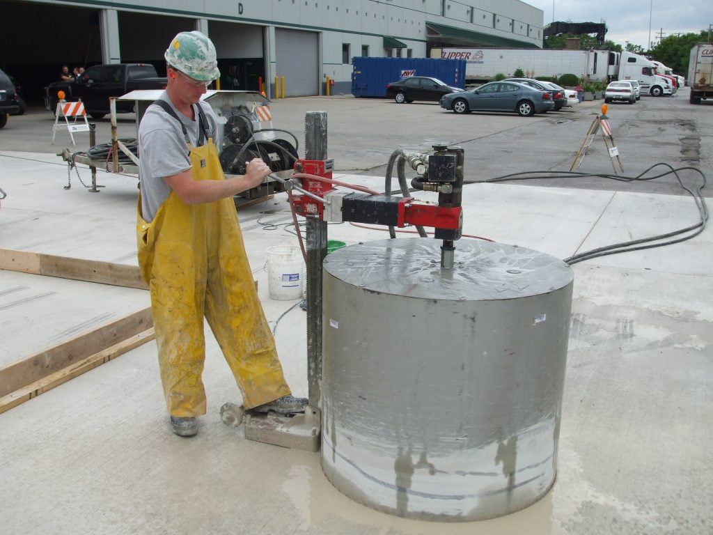 A man in yellow overalls is working on a concrete coring machine