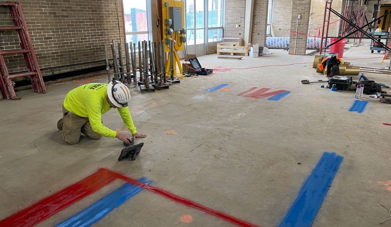 A construction worker is kneeling on the floor in a building under construction.