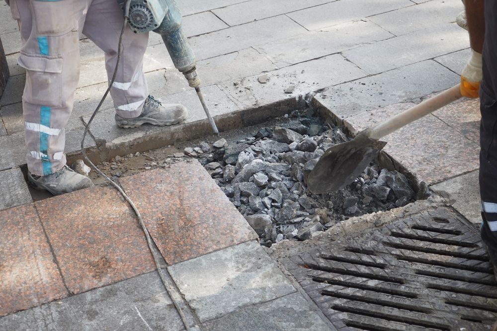 A man is using a hammer and a shovel to remove rocks from the ground.