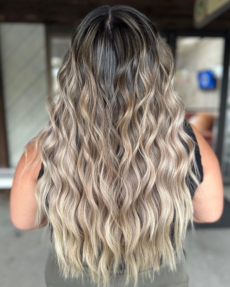 A woman with long wavy blonde hair is wearing a black tank top.