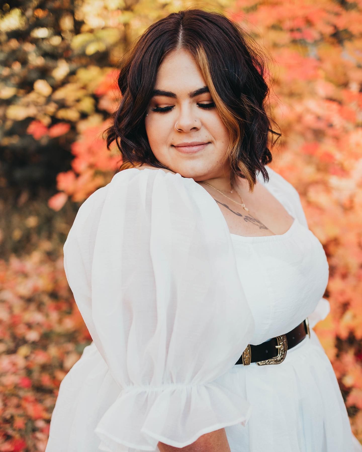 A woman in a white dress is standing in front of a bush with red leaves.