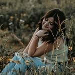 A woman is sitting in the grass with her eyes closed.