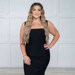 A woman in a black dress is standing in front of a white wall.