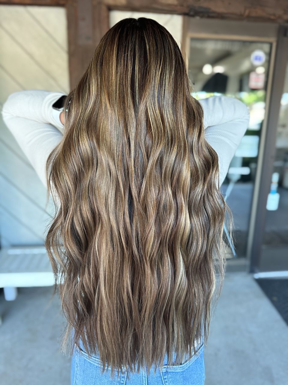 A woman with long wavy brown hair is standing in front of a door.