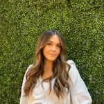 A woman is standing in front of a green hedge.