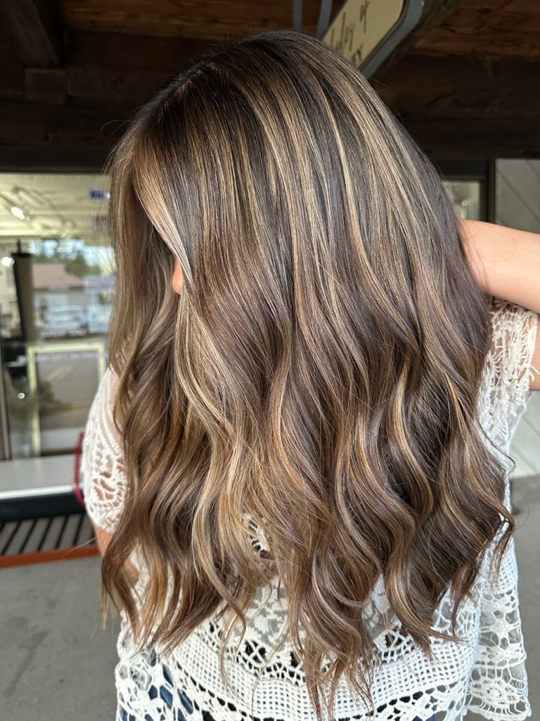 A woman with long brown hair is wearing a white lace top.