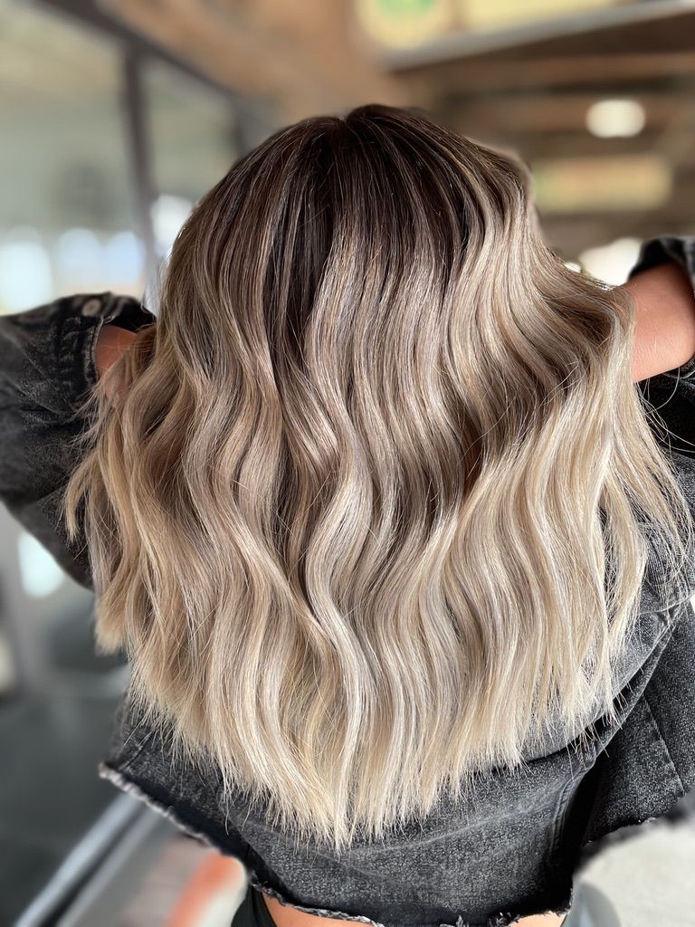 A woman with long wavy blonde hair is wearing a black jacket.