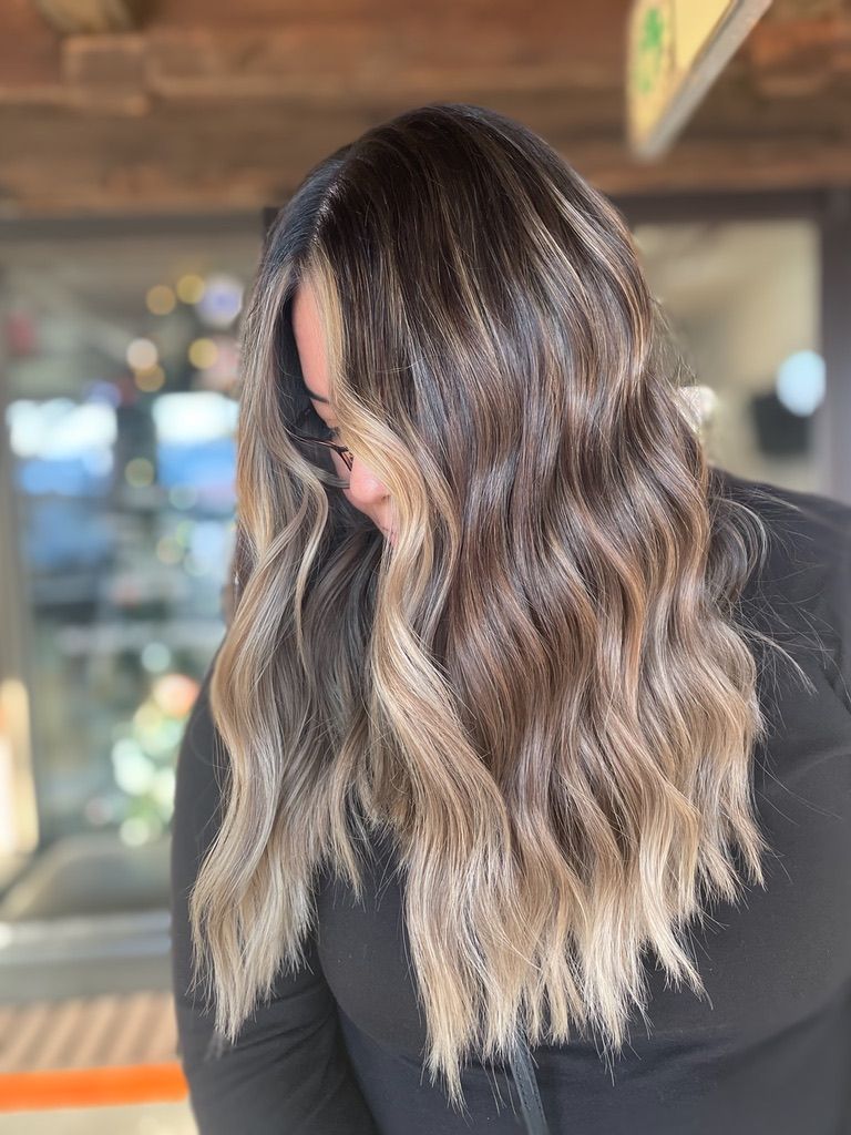 A woman with long brown hair is wearing a black shirt and looking down.
