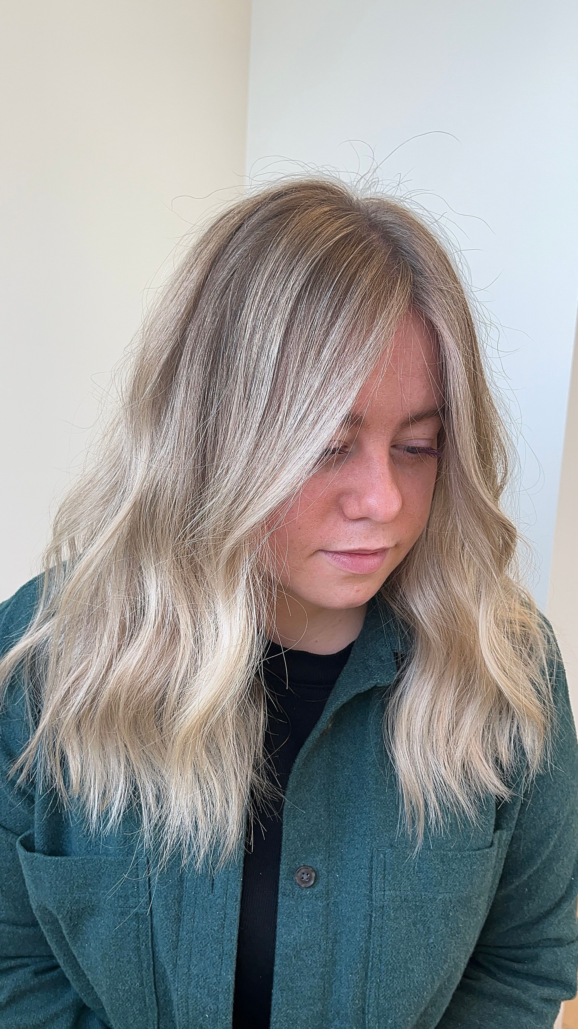 A woman with long blonde hair is wearing a green jacket.