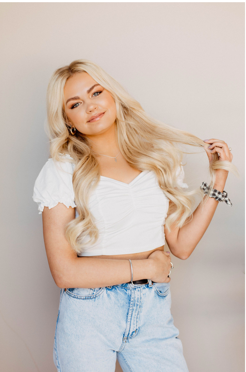 The woman is wearing a white crop top and blue jeans.