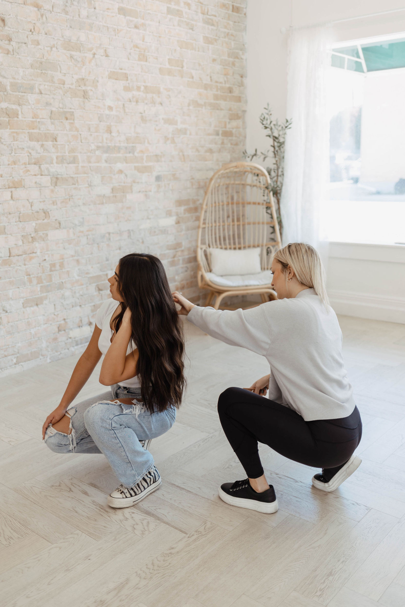 A woman is squatting down next to a woman sitting on the floor.