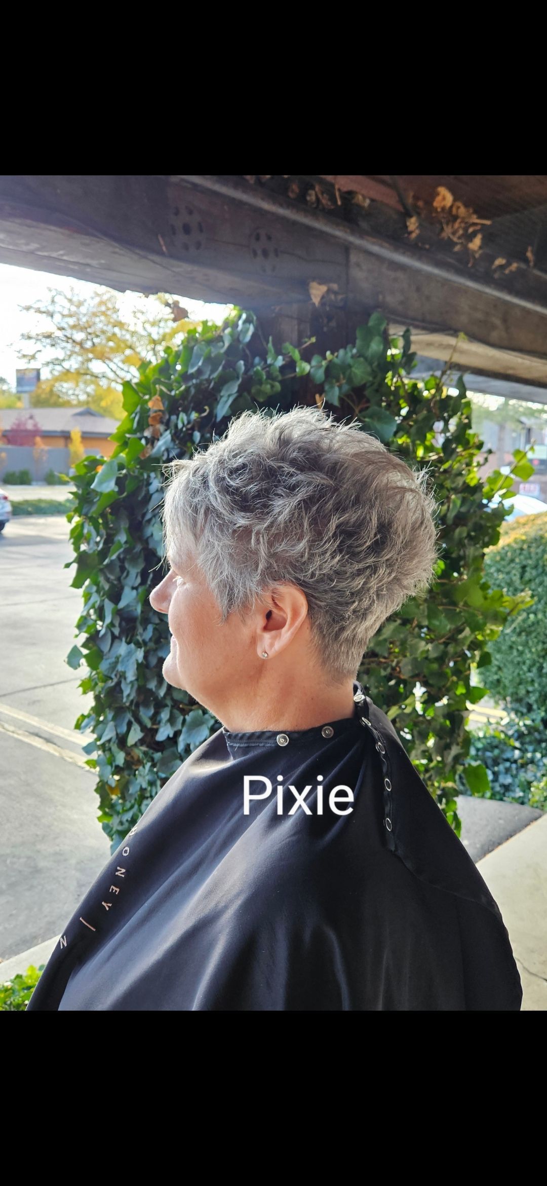 A woman with short gray hair is wearing a black cape.