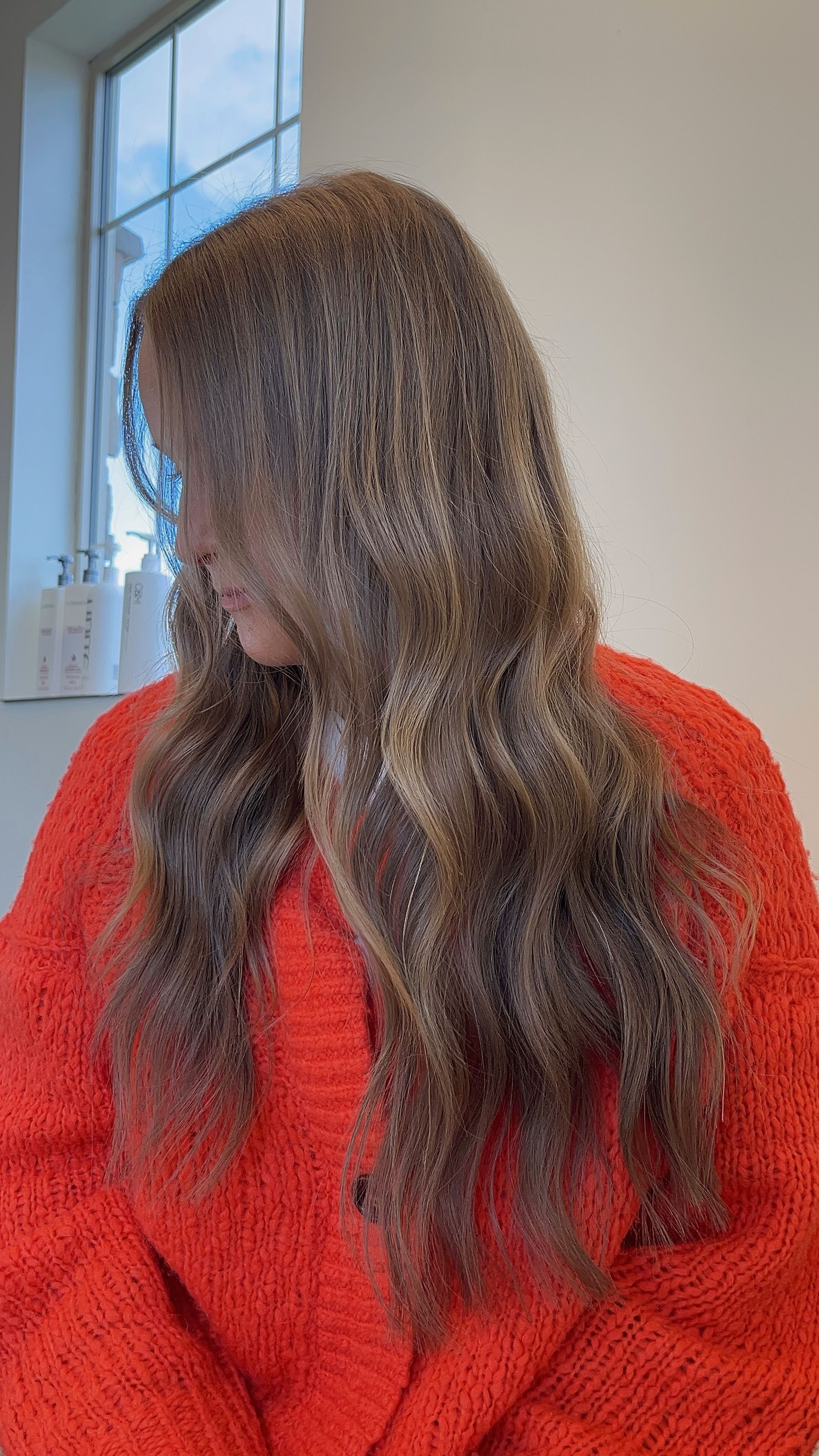 A woman in a red sweater is sitting in front of a window.