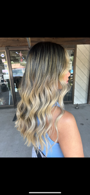 A woman with long blonde hair is standing in front of a building.