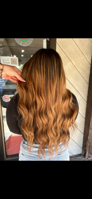 A woman with long wavy brown hair is standing in front of a window.