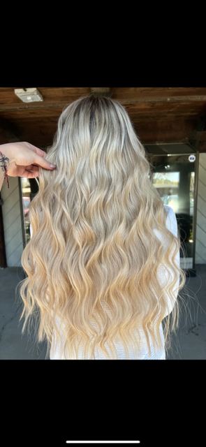 A woman with long blonde hair is getting her hair cut by a hairdresser.