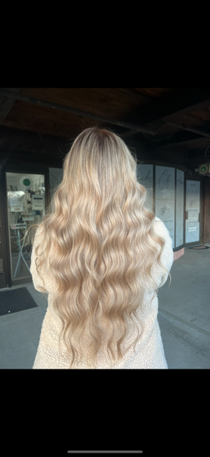 A woman with long blonde hair is standing in front of a building.