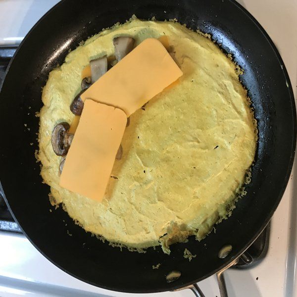 tofu omelette ingredients in cast iron skillet with cheese and mushrooms