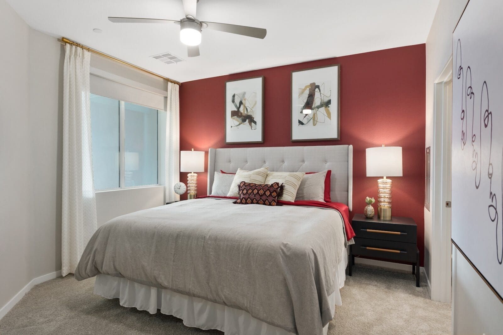Bedroom with red accent wall, bed, nightstands, art, and a window with sheer curtains at Echo Biltmore in Phoenix, AZ..