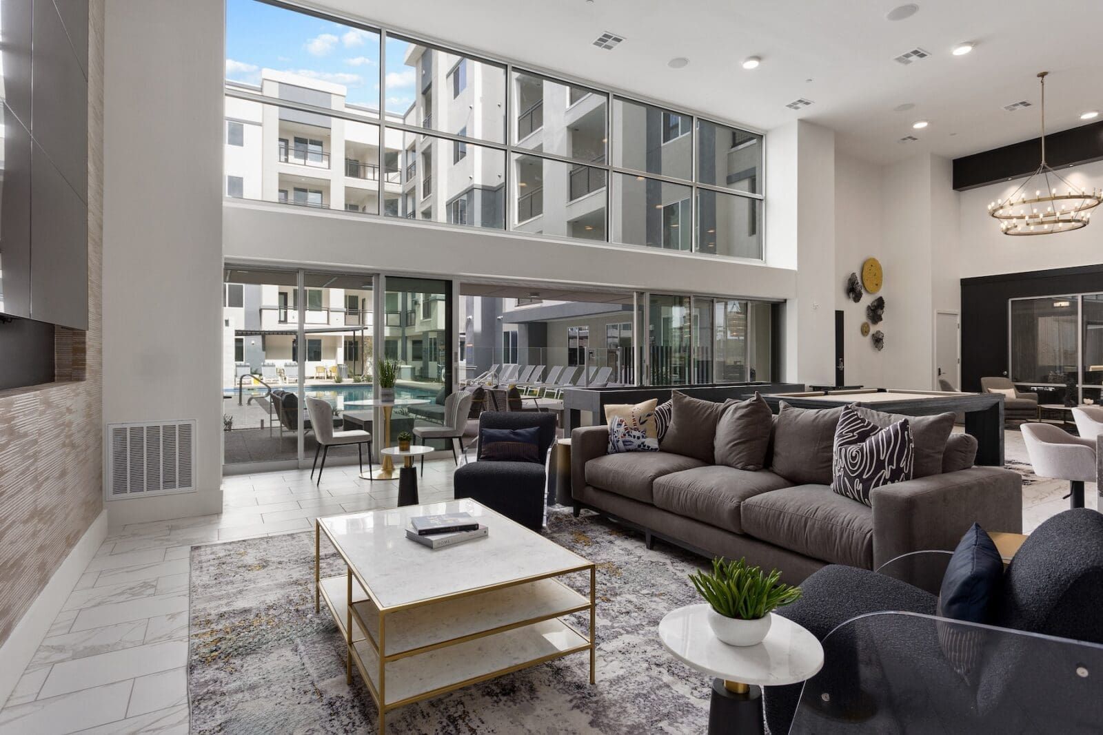 Lounge with a large sofa, chairs, and marble coffee table, with a view of a pool area and modern buildings outside at Echo Biltmore in Phoenix, AZ..