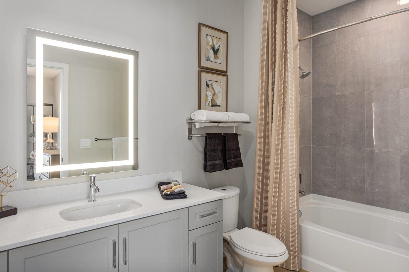 Modern bathroom with lighted mirror, grey vanity, and shower/tub with curtain at Echo Biltmore in Phoenix, AZ..