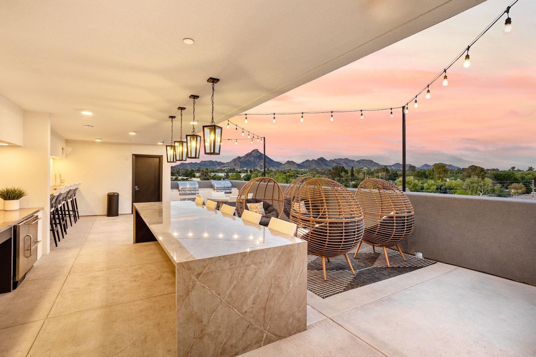 Rooftop patio with long marble table, chairs, string lights, and mountain view at sunset at Echo Biltmore in Phoenix, AZ..