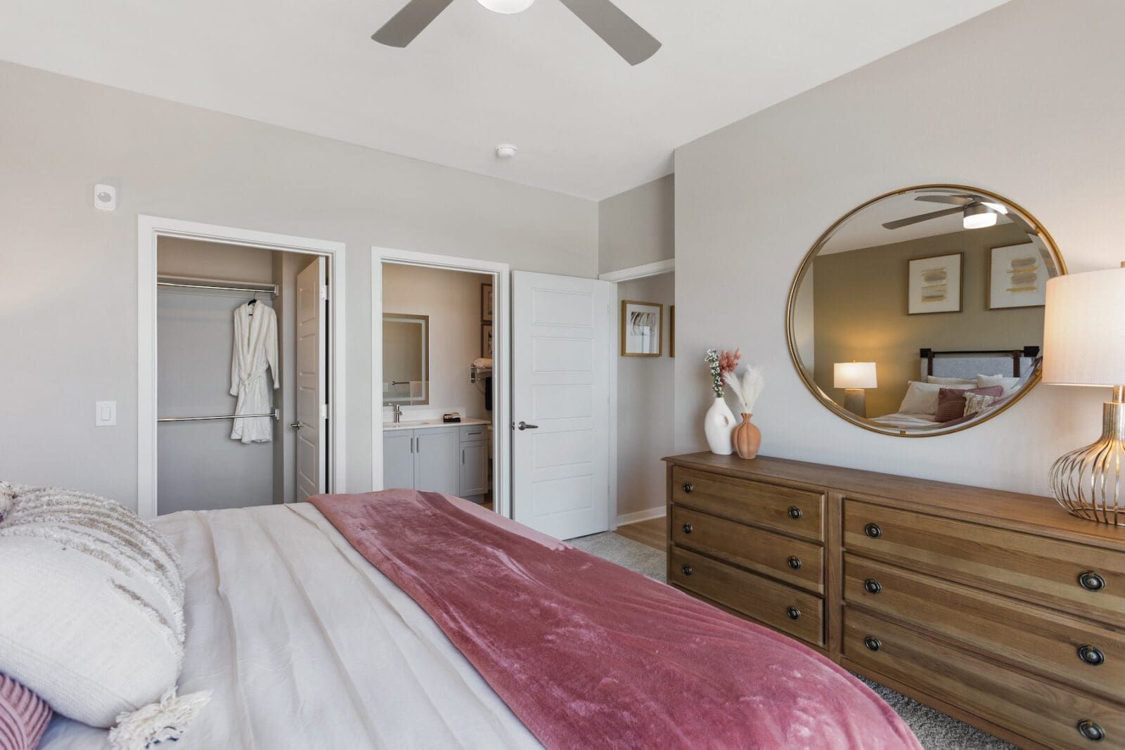 Bedroom with a bed, dresser, mirror, closet, and bathroom; neutral colors at Echo Biltmore in Phoenix, AZ..