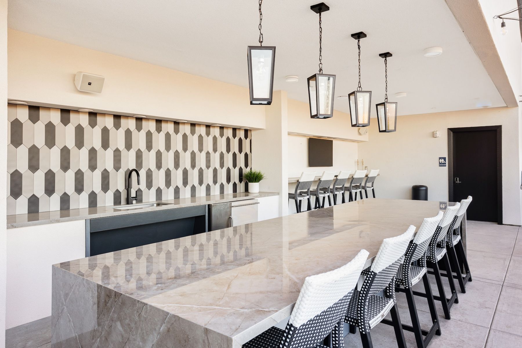 Outdoor kitchen with countertop seating, black and white patterned backsplash, and hanging pendant lights at Echo Biltmore in Phoenix, AZ..