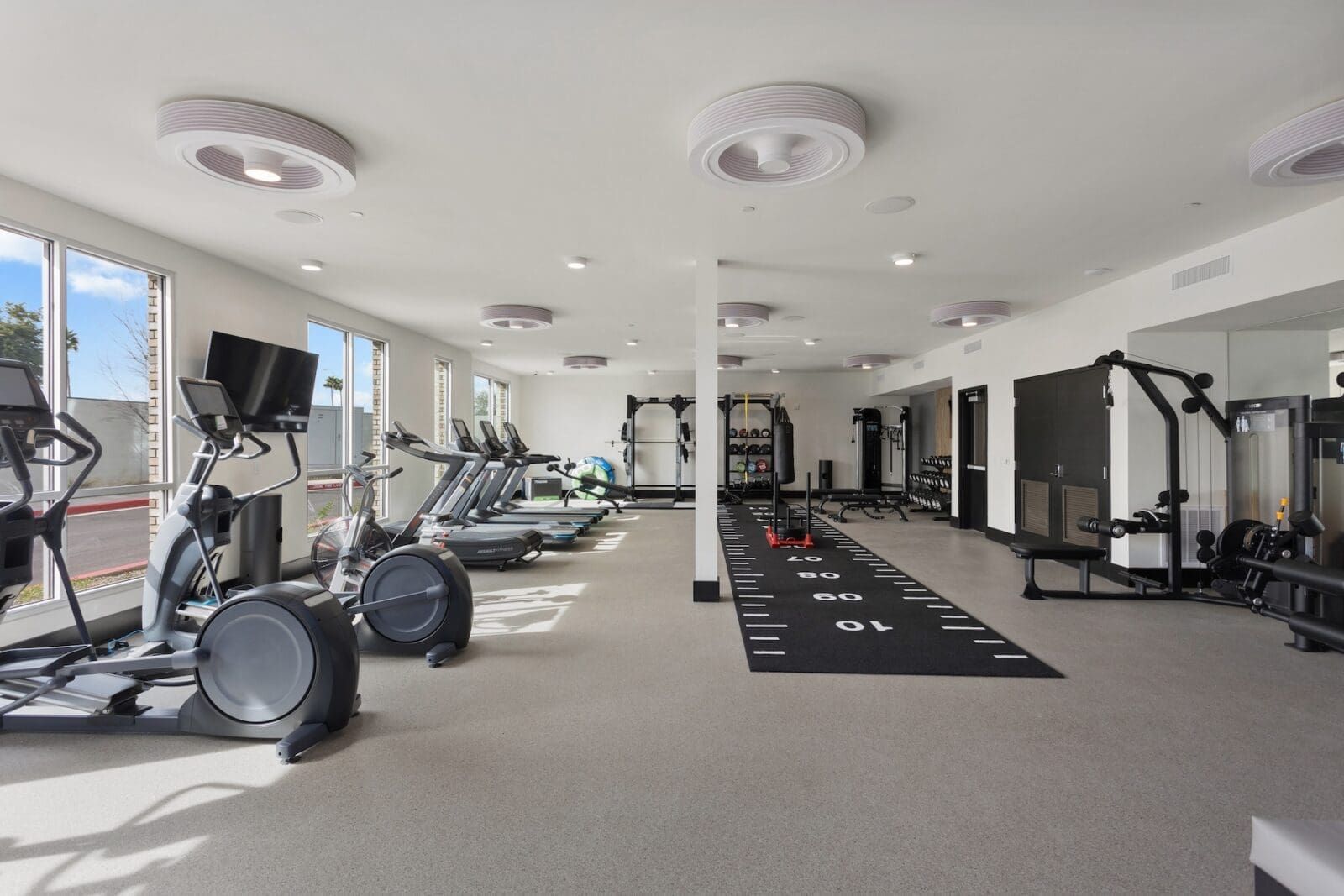 Gym interior with cardio and weight machines, bright white walls, and large windows at Echo Biltmore in Phoenix, AZ..